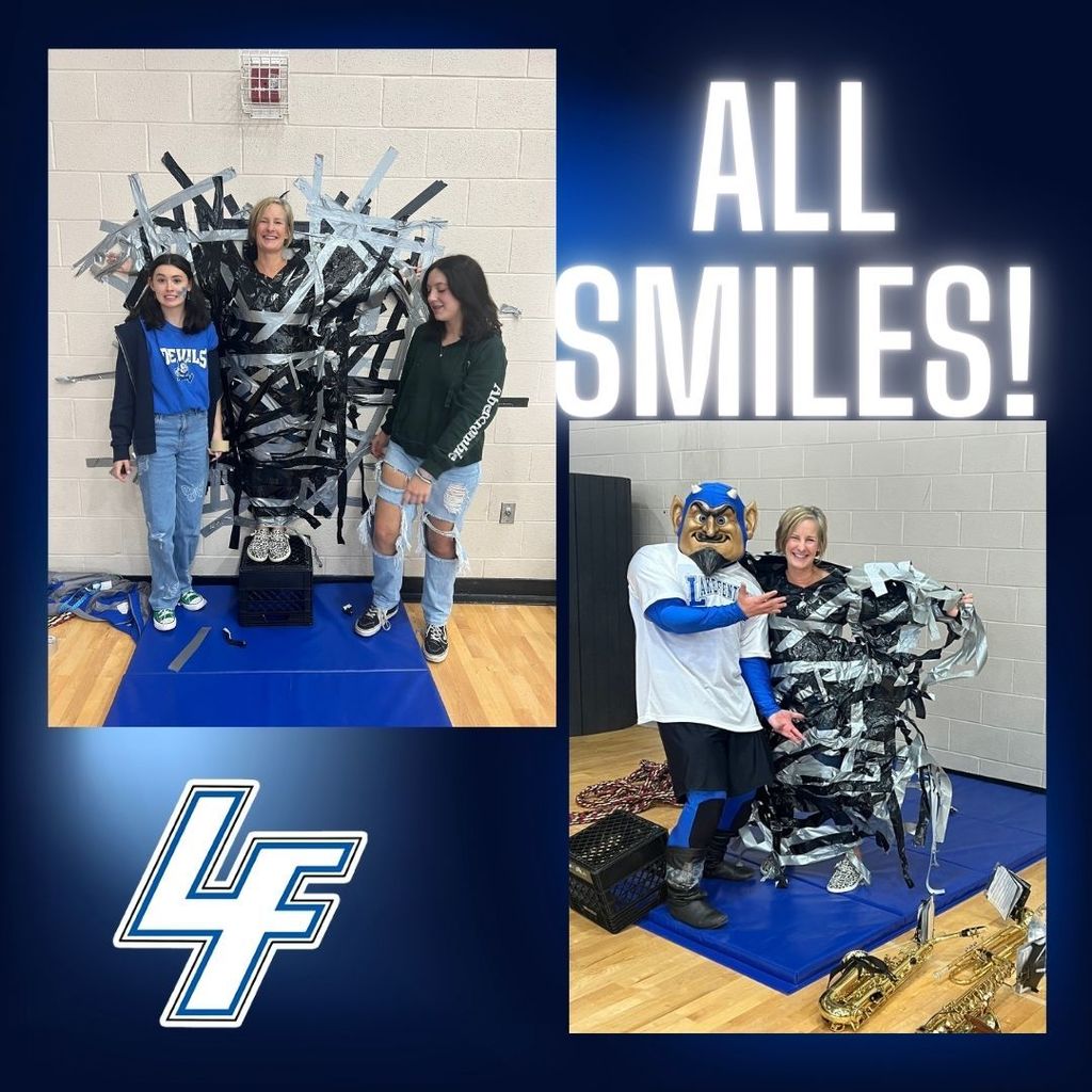 A teacher taped to the wall smiling and our mascot blue devil with her