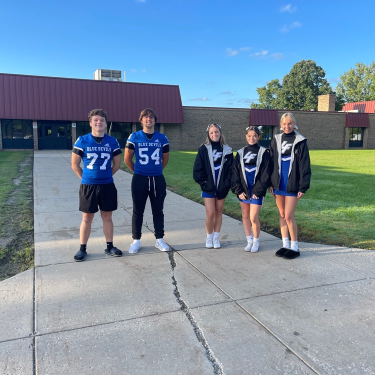 cheerleaders and football players posing in front of school