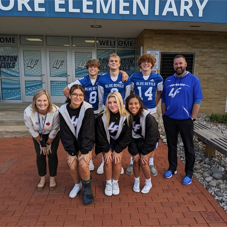 cheerleads and football players posing in front of school